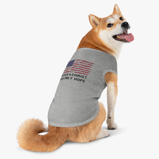 A Shiba Inu dog sitting on a white background wearing a gray sleeveless t-shirt. The shirt features a distressed American flag graphic and the text "JESUS * CHRIST OUR ONLY HOPE" in black.
