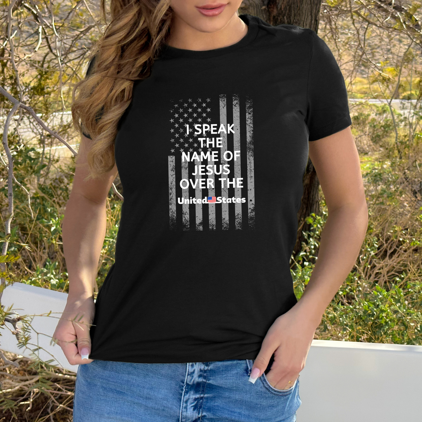 A black T-shirt featuring a white U.S. flag design, overlaid with white text that says "I Speak the Name of Jesus Over the United States.