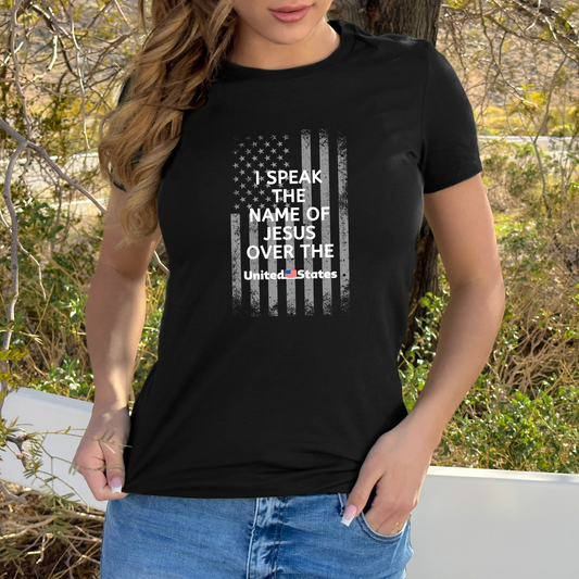 A black T-shirt featuring a white U.S. flag design, overlaid with white text that says "I Speak the Name of Jesus Over the United States.
